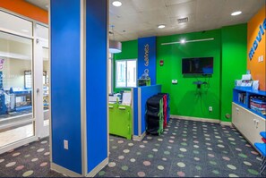 Ein helles Zimmer mit einer blauen und grünen Wand, einem an der Wand befestigten Fernseher und einer Theke mit dem Schild 'No Games'.