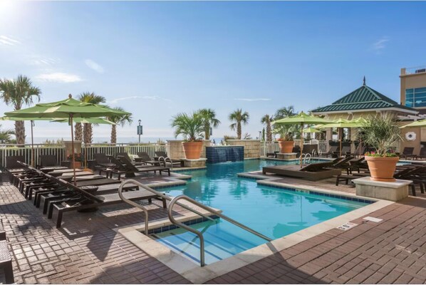 Ein Poolbereich mit Liegestühlen, Sonnenschirmen und freiem Blick auf das Meer.