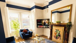 A living room with a blue sofa set, a coffee table, a fireplace with a framed picture, and a wall-mounted TV displaying a Netflix show. - Coastal Getaway 5-bed Sleeps 10 | DN35 (North East Lincolnshire)