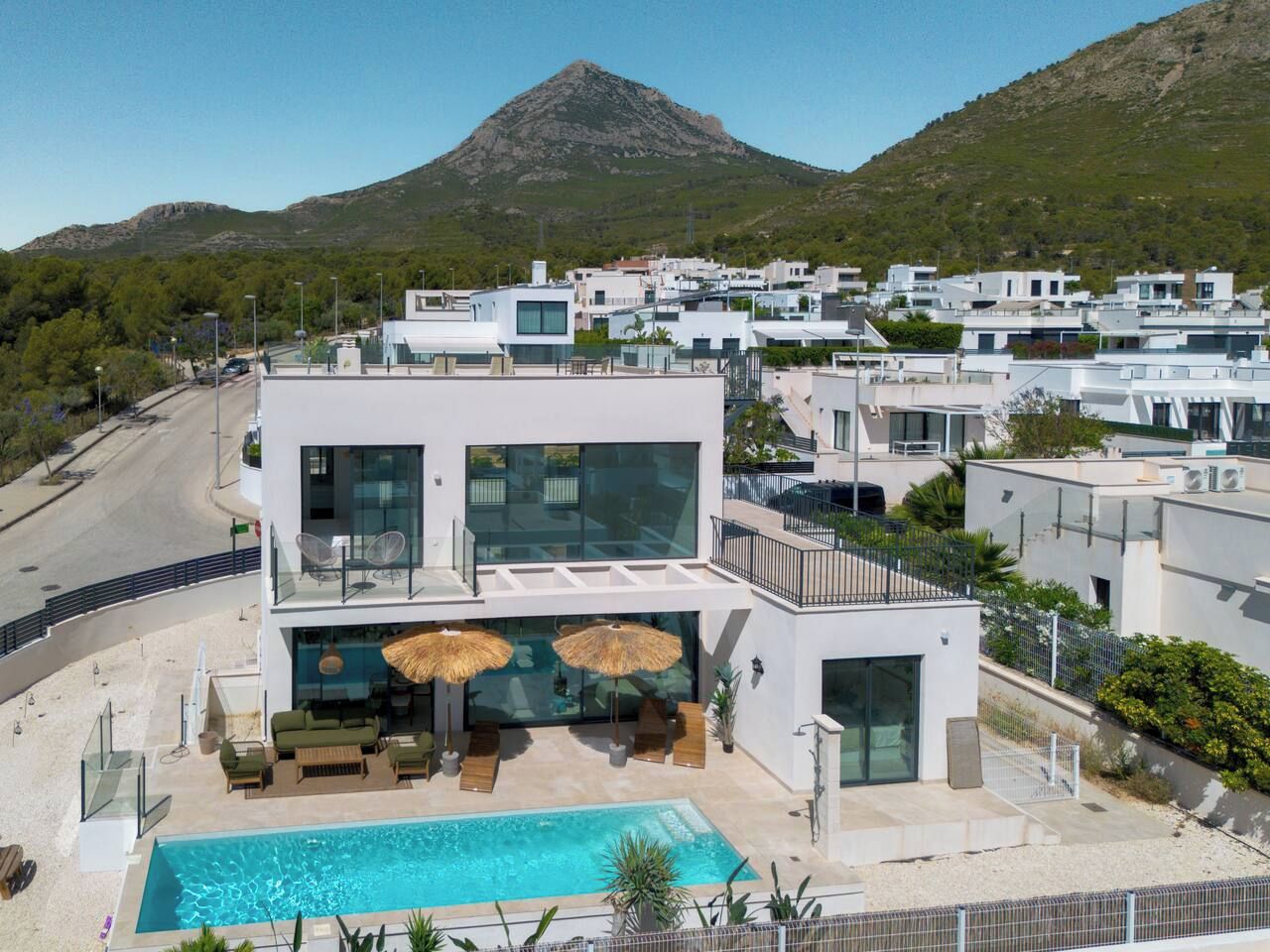 Un edificio moderno de dos pisos con piscina, asientos al aire libre y vista a la montaña.