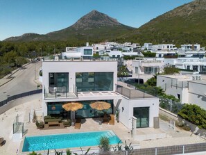 Een modern gebouw met twee verdiepingen, een zwembad, terras en uitzicht op een berg.