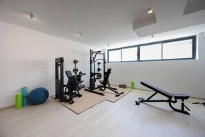 Et fitnessrum med træningsudstyr, en bænk og et stort vindue med naturligt lys.