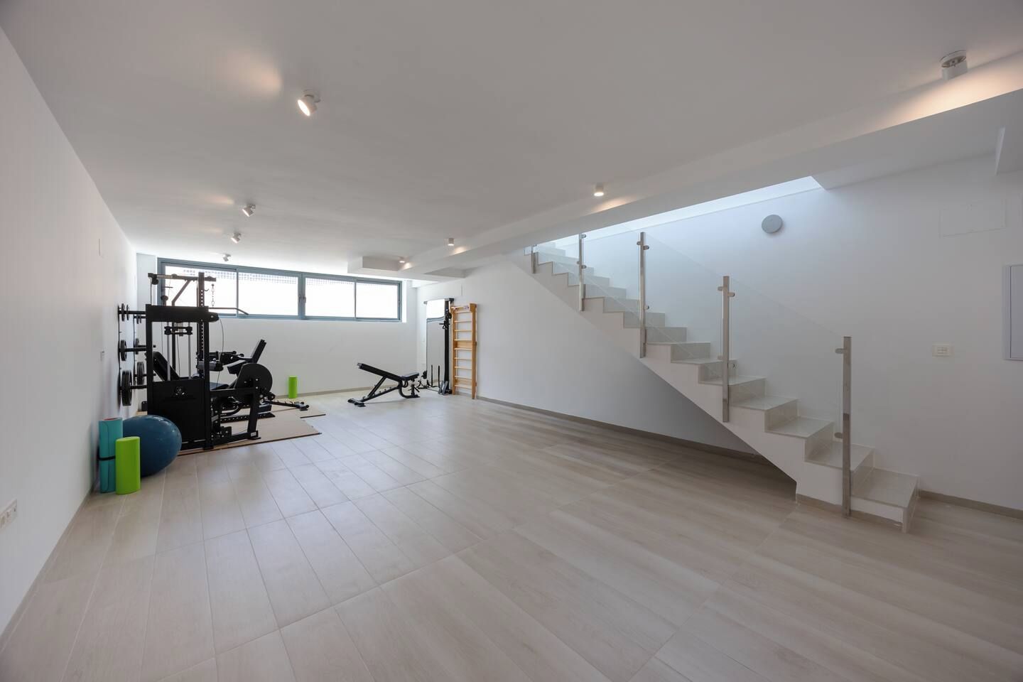 Ein geräumiges Zimmer mit Fitnessbereich, einer Treppe und einem großen Fenster, das für natürliches Licht sorgt.