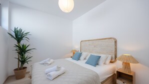 Un dormitorio con cama, mesita de noche, lámpara, planta en maceta y lámpara colgante.