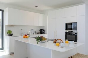 A modern kitchen with white cabinetry, a central island with fruits and breakfast items, and a Bosch oven. - Luxury Pool Villa by Fidalsa (Polop)