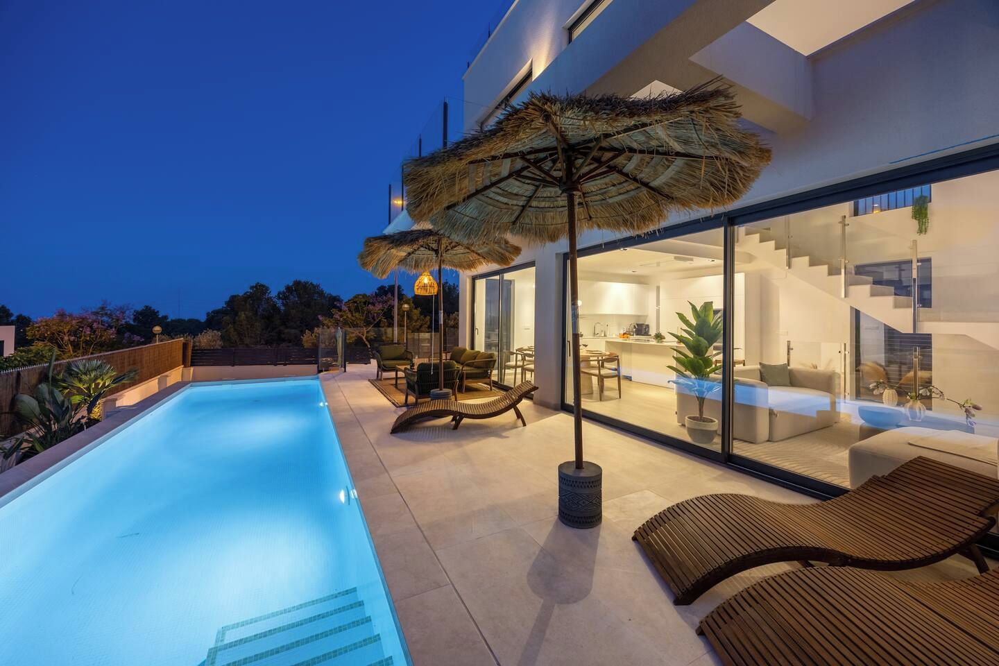 A modern house with a swimming pool, outdoor seating, and a glass-enclosed kitchen.