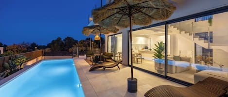 A modern house with a swimming pool, outdoor seating, and a glass-enclosed kitchen.