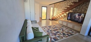 A modern living room with a sofa, a patterned rug, a television, and a stone wall. - Casa Duplex no Condominio Bella Arte (Aquiraz)