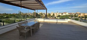 A rooftop terrace with a dining table and chairs, a pergola, and a view of surrounding buildings and greenery. - Casa Duplex no Condominio Bella Arte (Aquiraz)