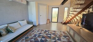 A modern living room with a sofa, a patterned rug, a TV, and a staircase leading to a balcony. - Casa Duplex no Condominio Bella Arte (Aquiraz)
