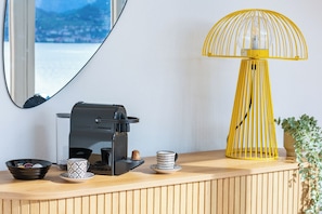A coffee maker, a cup, a bowl, and a yellow lamp on a wooden surface.