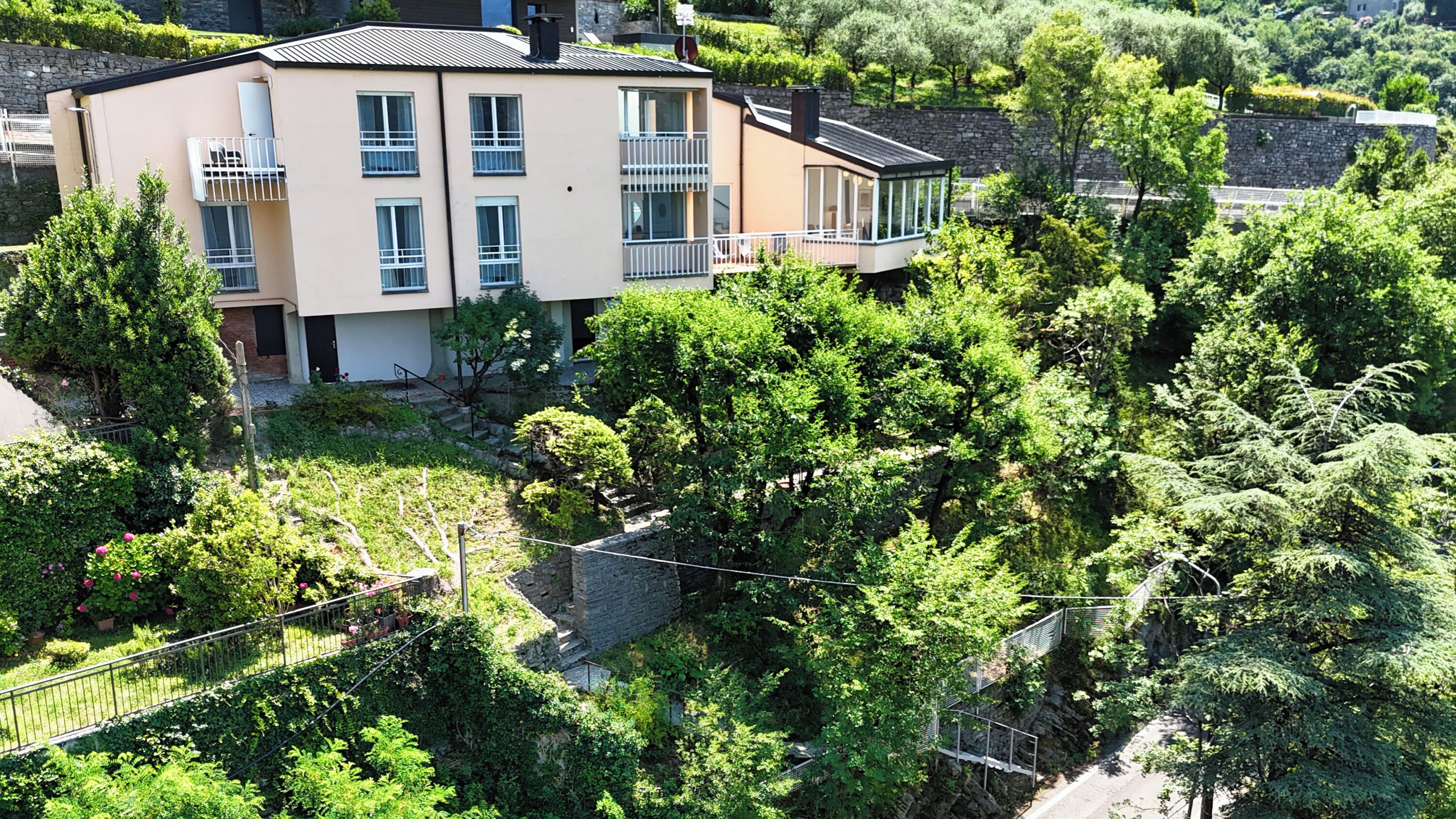 Ein mehrgeschossiges Gebäude mit Balkonen, umgeben von üppiger Vegetation und Steinmauern.