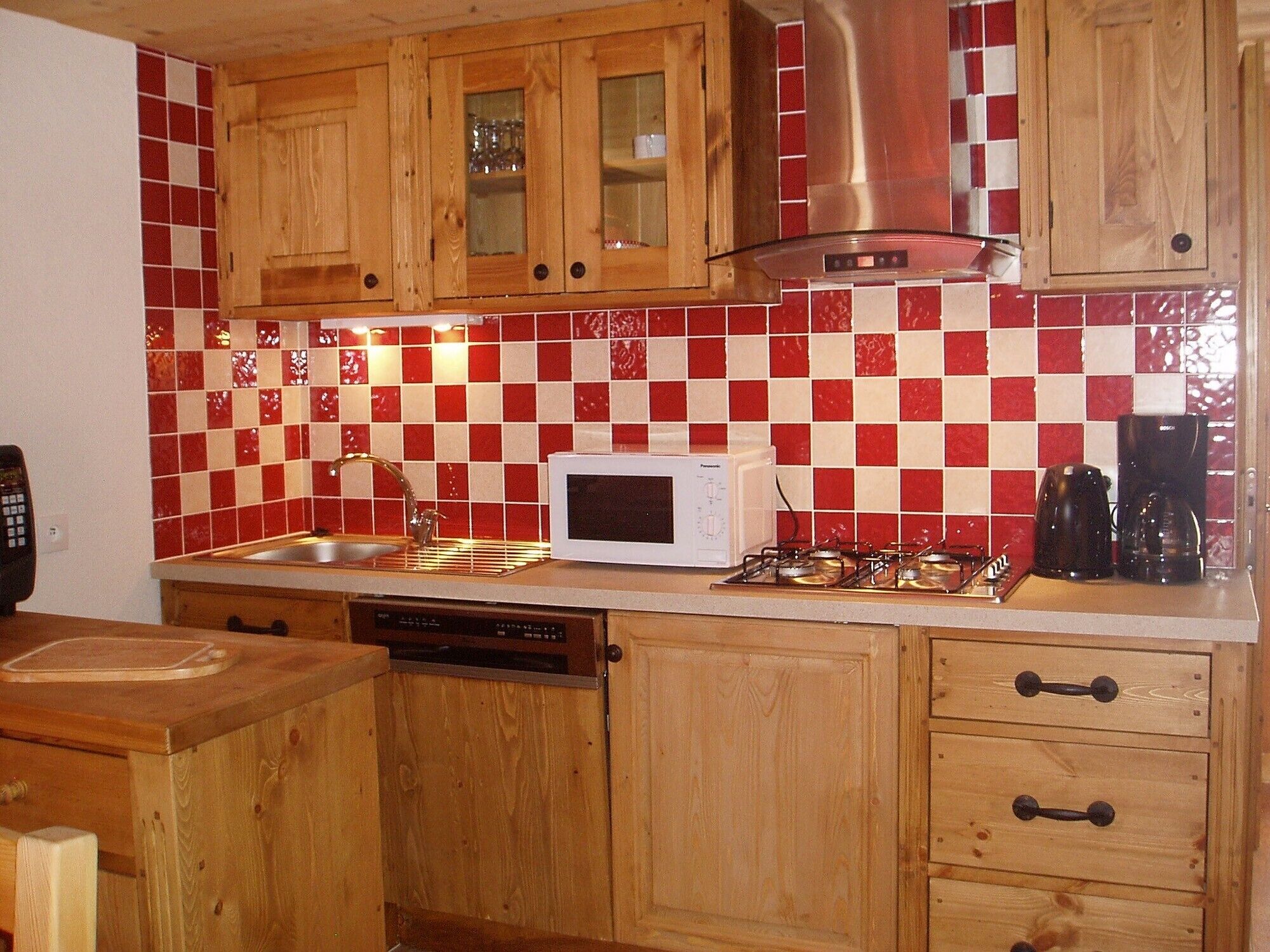 A kitchen with wooden cabinets, a red and white checkered backsplash, a white microwave, a gas stove, and a coffee maker.