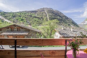 Blick auf Berge mit traditionellen Steinhäusern, einem Holzzaun und einem rosafarbenen Tisch mit Blumen.