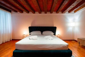 Ein Hotelzimmer mit einem großen Bett, Holzbalkendecke, zwei Nachttischen und einer Stehlampe.