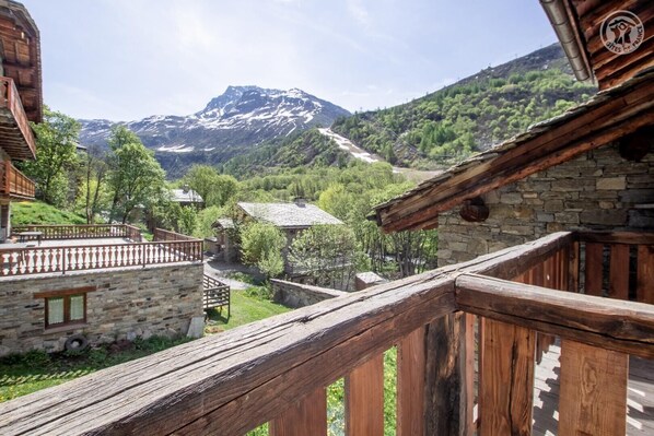 Ein rustikaler Holzbalkon mit Blick auf eine gebirgige Landschaft und Steinhäuser.