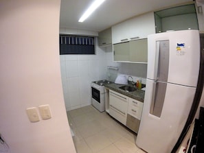 Eine kleine Küche mit weißen Schränken, einem Herd, einem Spülbecken und einem Kühlschrank.