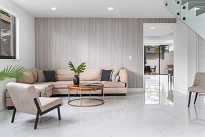 Ein modernes Wohnzimmer mit einem beigen Sofa, einem runden Couchtisch und einem Sessel.