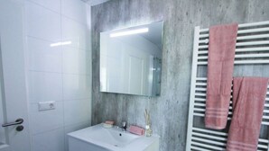Ein Badezimmer mit weißem Waschtisch, einem Spiegel, einem Handtuchhalter mit Handtüchern und einer Betonwand.