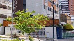 Un edificio a più piani con facciate in mattoni e piastrelle, un lampione e un'area recintata con alberi.