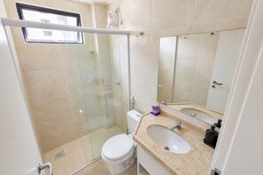 A bathroom with a glass shower enclosure, a toilet, a sink, and a large mirror. - Flat 2 Quartos no Melhor Local de Fortaleza (Fortaleza)