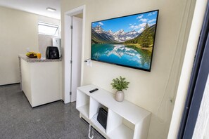 Ein Hotelzimmer mit Küchenzeile, einem montierten Fernseher, der einen Bergsee zeigt, und einer kleinen Pflanze auf dem Konsolentisch.