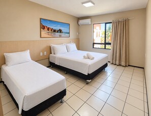 Habitación de hotel con dos camas, un cuadro de una playa, un equipo de aire acondicionado y una ventana con cortinas.