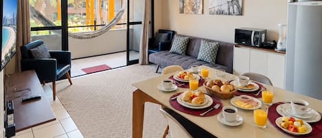 Una habitación de hotel moderna con comedor, sofá, televisor y balcón con hamaca.
