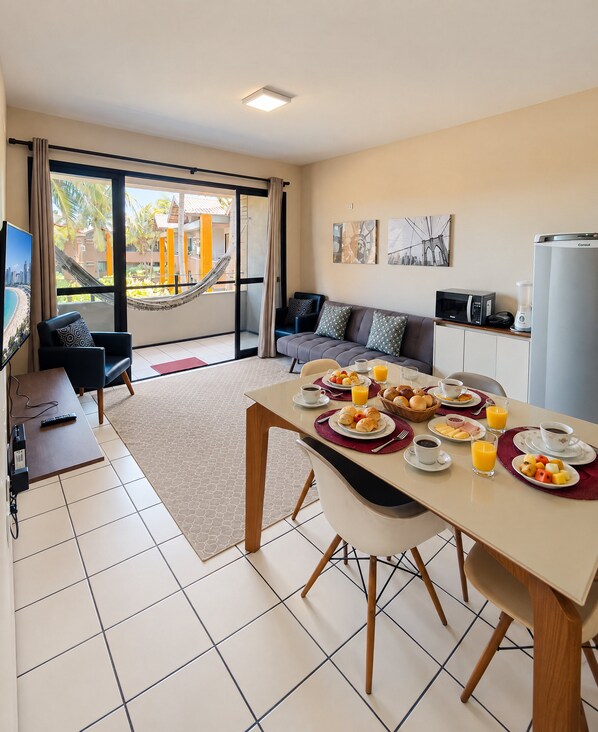 Una habitación de hotel moderna con comedor, sofá, televisor y balcón con hamaca.