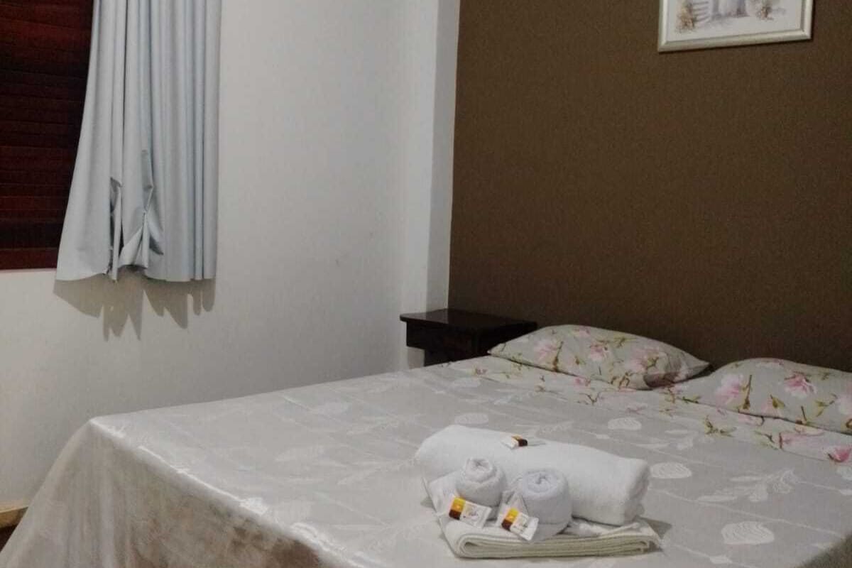 A hotel room with a bed, a nightstand, a framed picture on the wall, and a window with curtains.