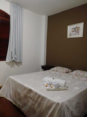 A hotel room with a bed, a nightstand, a framed picture on the wall, and a window with curtains. - Pousada Santana (Sabará)