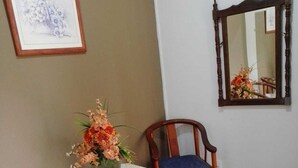 Une pièce comprenant deux chaises en bois, une petite table recouverte d’une nappe blanche et un miroir accroché au mur.