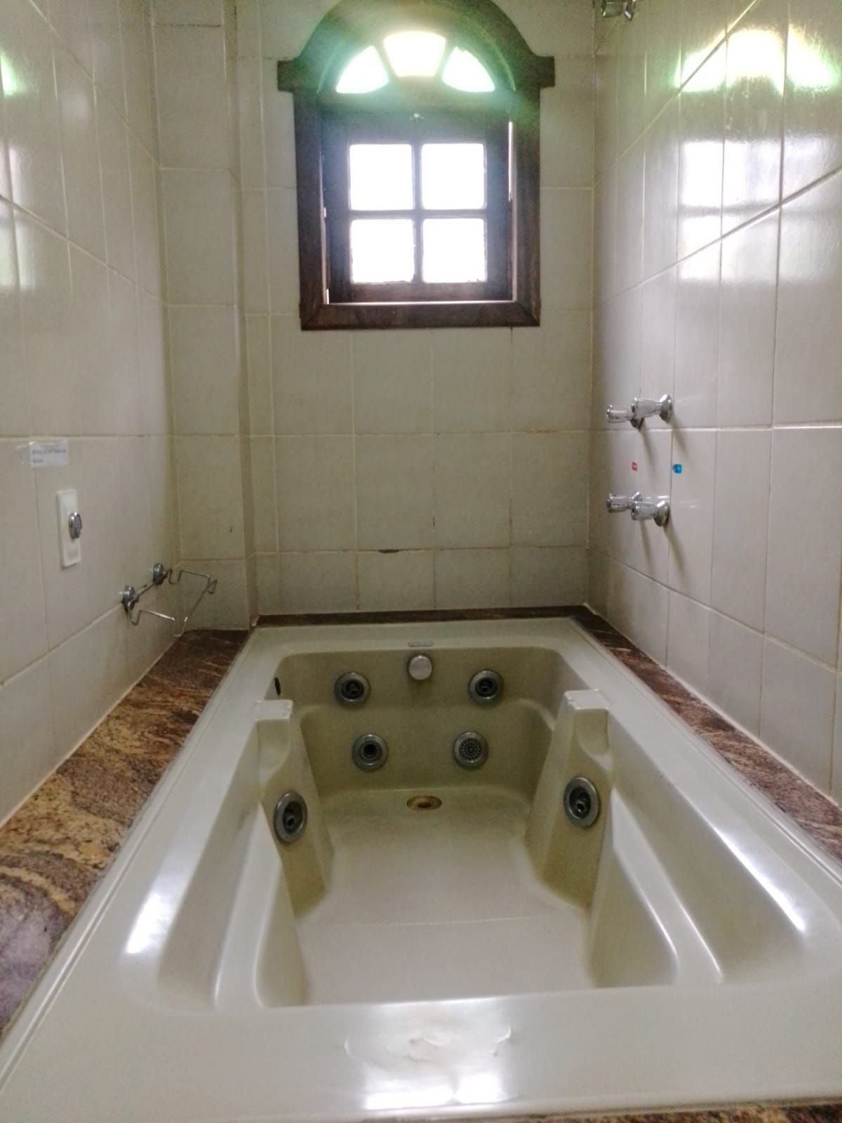 Un baño con una bañera grande, una ventana encima y paredes con azulejos.