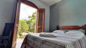 Une chambre avec un lit, une fenêtre avec des volets et une vue sur la verdure.