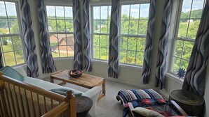 A sunroom with a view of a green landscape, a wooden bench, a table with a bowl of fruit, and a patterned sofa. - Lake Anna Waterfront Family & Pet Friendly Retreat! With 5+ BRs 4 BAs. (Spotsylvania Courthouse)