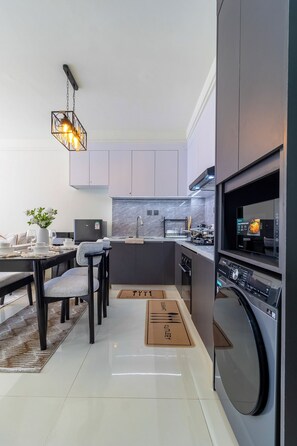 A modern kitchen with a built-in oven, a dining area with a table and chairs, and a hanging light fixture. - Luxury 1BR in Westlands | Fast Wi-Fi | Self Check-in | Near Sarit & Westgate (Nairobi)
