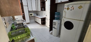 A compact kitchen with white cabinets, a microwave, a water dispenser, and a refrigerator. - Ape Familia 200 Metros da Feirinha Beira mar 502 (Fortaleza)
