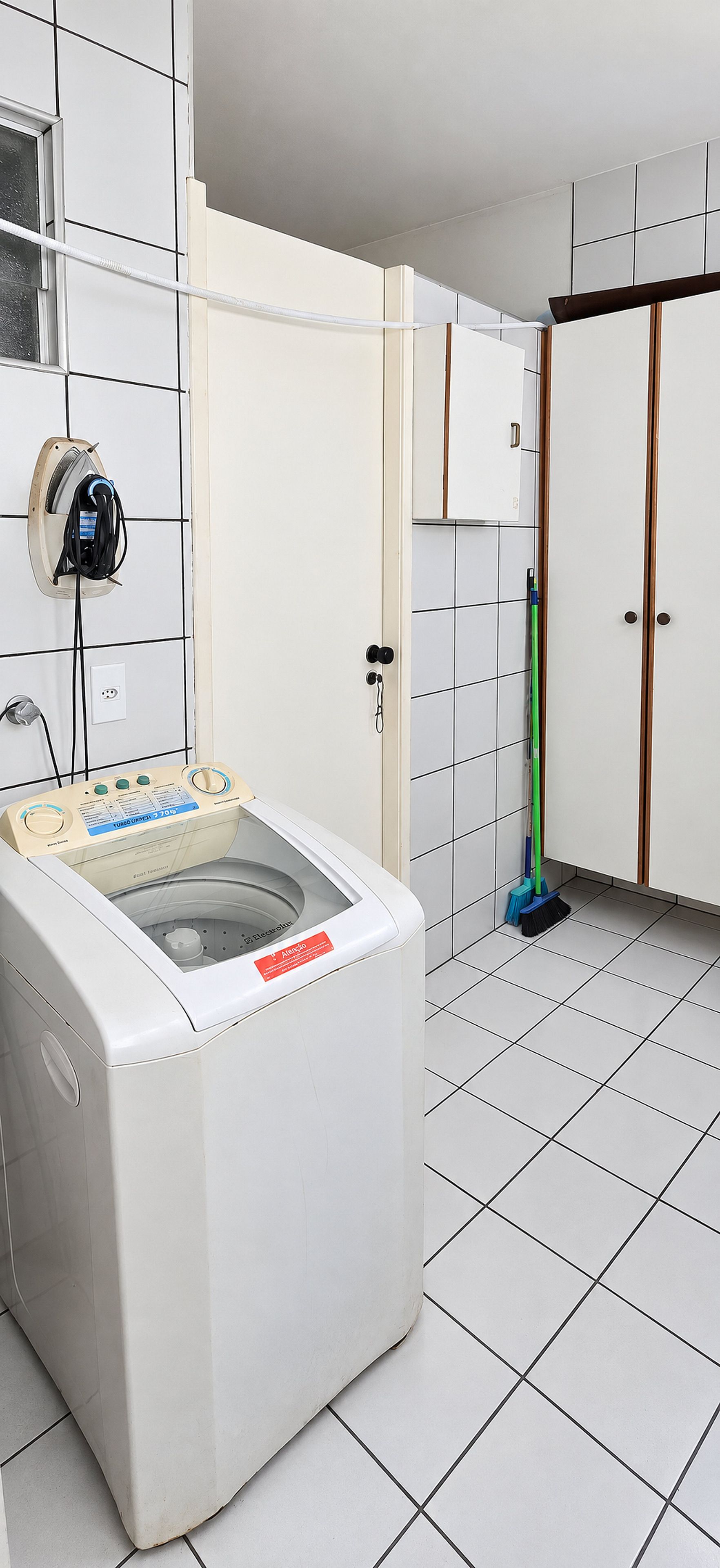 A laundry room with a front-loading washing machine, a mop, and a door with a handle.