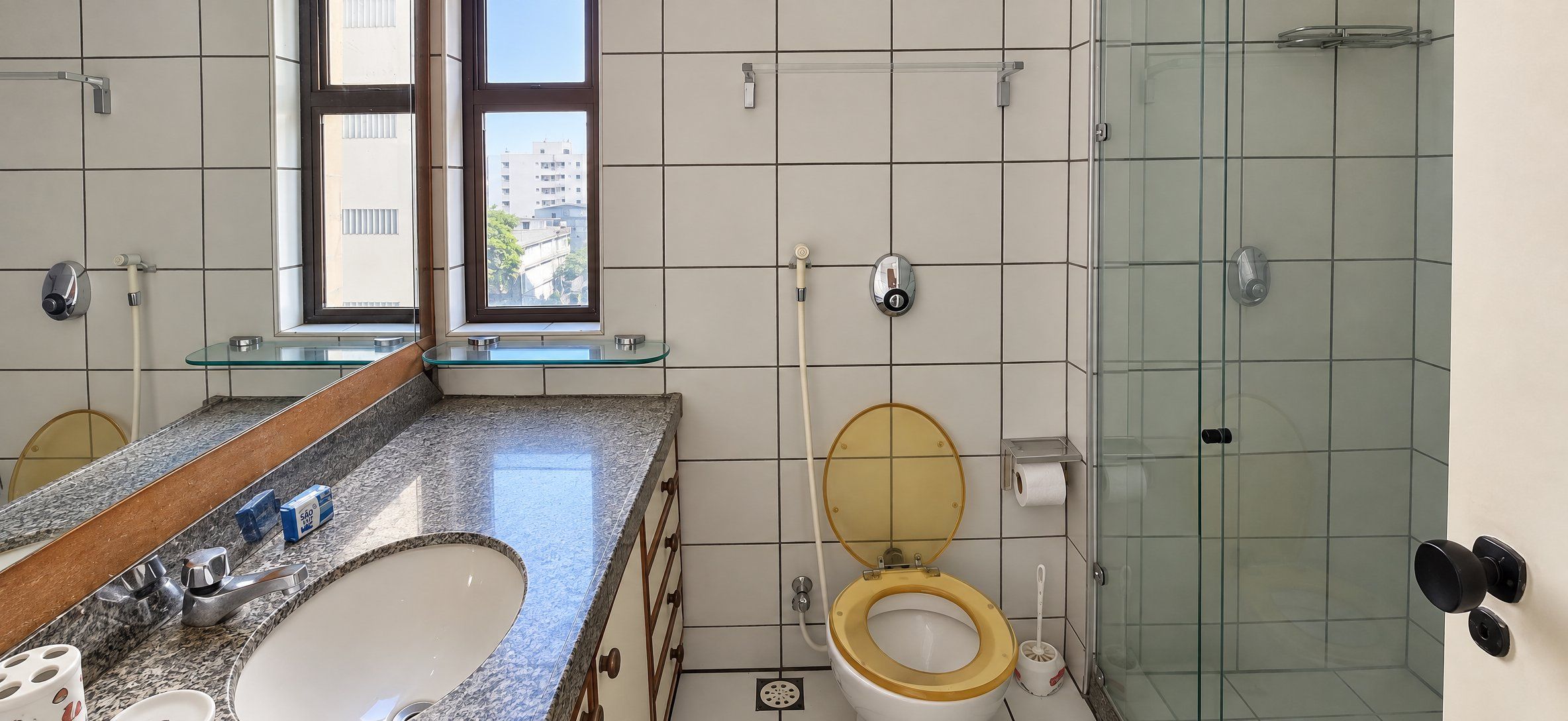 Casa de banho moderna com chuveiro em cabine de vidro, lavatório duplo e sanita com assento dourado.