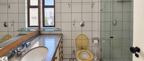 Casa de banho moderna com chuveiro em cabine de vidro, lavatório duplo e sanita com assento dourado.