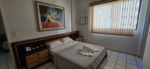 A hotel room with a bed, a nightstand, a painting, a thermostat, and a window with blinds. - Ape Familia 200 Metros da Feirinha Beira mar 502 (Fortaleza)
