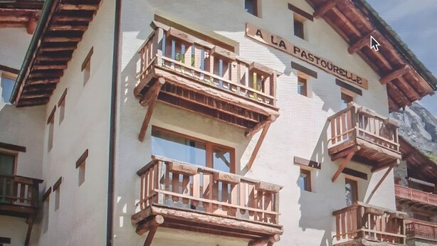 Un edificio de varios pisos con balcones, un letrero que dice 'LA PASTORELLE' y asientos al aire libre.