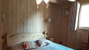 Una habitación con paneles de madera, una cama, un lámpara colgante y un ventanal con cortinas.
