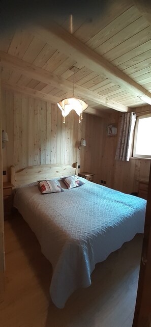 Ein Zimmer mit Holzwänden, einem Bett, einer Hängelampe und einem Fenster mit Vorhängen.