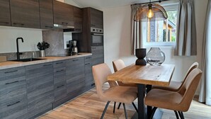 A modern kitchen with dark wood cabinets, a wooden dining table, and a hanging light fixture. - Holiday Home in Maarn With Wi-fi (Maarn)