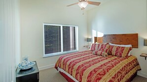 Ein Schlafzimmer mit einem großen Bett, einem Deckenventilator, einem Fenster mit Jalousien und einem Nachttisch mit Lampe.
