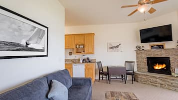 A living room with a gray sofa, a coffee table, a fireplace, a TV mounted on the wall, and a ceiling fan.