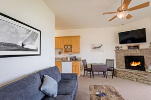 A living room with a gray sofa, a coffee table, a fireplace, a TV mounted on the wall, and a ceiling fan. - Spyglass inn (Shelter Cove)