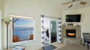 A living room with a stone fireplace, a television mounted above it, and a view of the ocean through a large window.