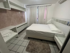 Ein Schlafzimmer mit Bett, Nachttisch, einem kleinen Teppich und einem Fenster mit Vorhängen.